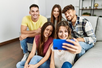 Group of young friends smiling happy make selfie by the smartphone sitting on the sofa at home.