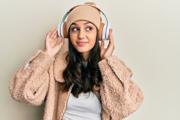 Young hispanic woman listening to music using headphones smiling looking to the side and staring away thinking.