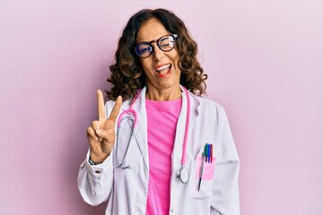 Middle age hispanic woman wearing doctor uniform and glasses smiling with happy face winking at the...