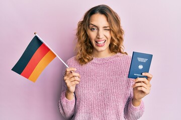 Young caucasian woman holding germany flag and passport winking looking at the camera with sexy...