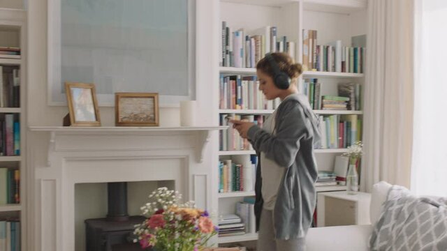 happy young woman dancing at home having fun enjoying funky hip hop dance moves practicing in living room using smartphone