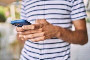 Young hispanic man using smartphone at street