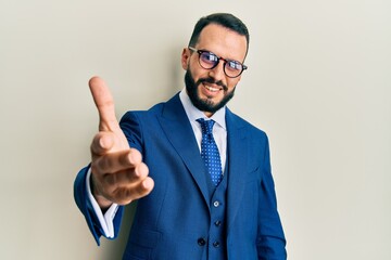 Young man with beard wearing business suit and tie smiling friendly offering handshake as greeting and welcoming. successful business.