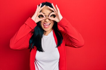 Beautiful hispanic woman with nose piercing wearing casual look and glasses doing ok gesture like...