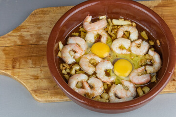 Shrimps or prawns in garlic olive oil in a crock pot, spanish appetizer on a wooden board. Typical spanish tapa. Dark rustic style food. Gambas al ajillo.