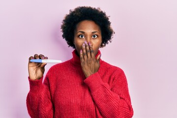 Young african american woman holding thermometer covering mouth with hand, shocked and afraid for...