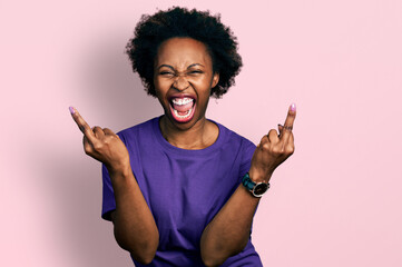 African american woman with afro hair wearing casual purple t shirt showing middle finger doing...