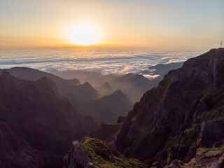 Spectacular landscape view of sunrise rising above sea of clouds surrounded with volcanic mountains.