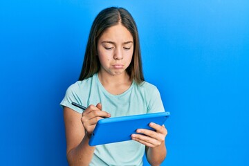 Beautiful brunette little girl using touchpad drawing on screen depressed and worry for distress,...
