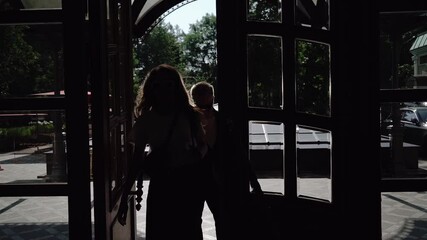 Man opens front door and lets woman through. Couple walks into a building.