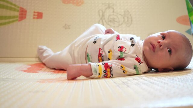 Baby learn head control, 2 month old baby boy lifting head lying on tummy on activity play mat at home.