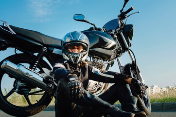 A middle-aged woman sits near her motorcycle and smiles. The concept of an active lifestyle at any age.