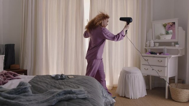 funny woman dancing in bedroom singing karaoke with hair dryer enjoying weekend morning having fun celebrating carefree lifestyle wearing pajamas at home