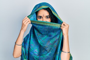 Young indian woman wearing sari covering head and face, doing elegant pose with traditional scarf