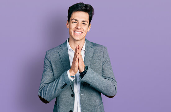 Young hispanic man wearing business clothes praying with hands together asking for forgiveness smiling confident.