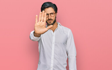 Young hispanic man wearing business shirt and glasses doing stop sing with palm of the hand....