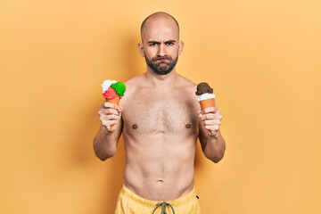 Fototapeta premium Young bald man wearing swimwear holding two ice cream cones skeptic and nervous, frowning upset because of problem. negative person.