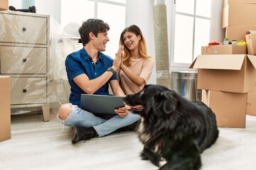 Young caucasian couple using laptop sitting on the floor with dog at new home.