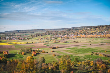 Panoramic view of an autumnal countryside: colorful meadows and trees, fields and forested hills of the Schönbuch natural reserve in the background.