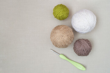 Balls of multicolored woolen threads and a crochet hook. Hobby, needlework. Natural colors and materials. Copy space. Flat lay