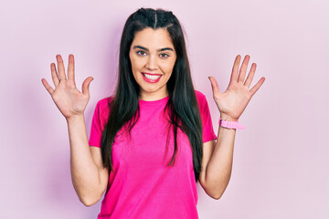 Young hispanic girl wearing casual pink t shirt showing and pointing up with fingers number ten while smiling confident and happy.