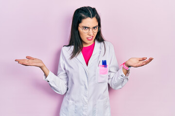 Young hispanic girl wearing scientist uniform clueless and confused expression with arms and hands...