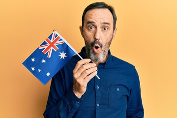 Middle age hispanic man holding australian flag scared and amazed with open mouth for surprise,...
