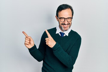 Middle age hispanic man wearing casual clothes and glasses smiling and looking at the camera pointing with two hands and fingers to the side.