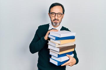 Middle age hispanic man holding a pile of books puffing cheeks with funny face. mouth inflated with air, catching air.