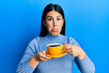 Beautiful brunette woman drinking a yellow cup of black coffee depressed and worry for distress, crying angry and afraid. sad expression.