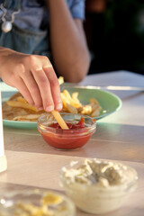 Child holds french fries in hand and puts on ketchup to eat, child eats fries served on the table in a restaurant
