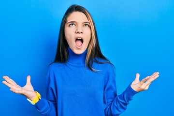 Young brunette girl wearing turtleneck sweater crazy and mad shouting and yelling with aggressive expression and arms raised. frustration concept.