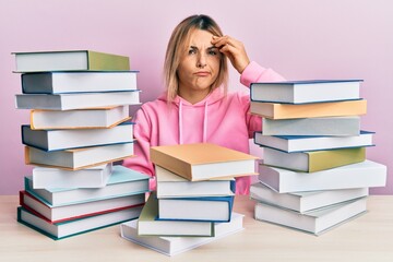 Young caucasian woman sitting on the table with books worried and stressed about a problem with hand on forehead, nervous and anxious for crisis