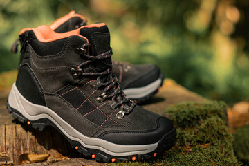 Closeup on pair of dark grey hiking boots on a natural raw wood in the woodland. Selective focus on dark shoes with ankle support for walking, surrounded by nature.