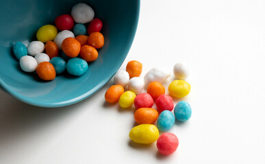 Colorful little candies spilled out of a blue bowl, isolated on a white background. Top view. Space for text