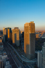 青空を背景に浜松町から汐留方向を見た夕陽にオレンジ色に染まるビル群と谷間を走る交通網