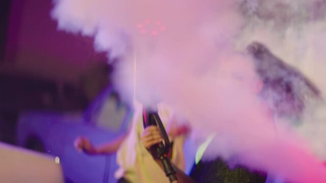 Mini smoke gun on the hand of beautiful sexy crazy girl . Girls dancing , partying inside  garage with old vintage cars . Dry Fog device in hand . Female dancer spraying, shooting smoke all around