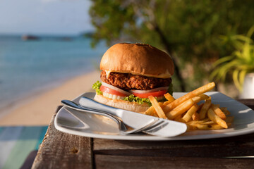 Large hamburger and chips served on a cafe table with sea views. Vacation and fast food