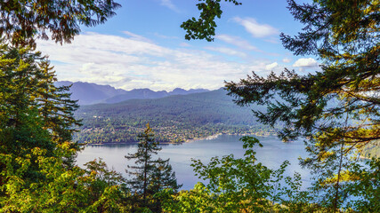 Looking through trees across scenic Burrard Inlet towards the town of Deep Cove, BC, from Burnaby...
