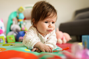 Fototapeta premium Close up on baby small caucasian girl five months old lying belly down on tummy at home in summer day playing with toy childhood concept looking to the side alone