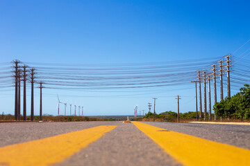 pista asfaltada com sinalização amarela e postes as margens com fios de alta tensão cruzando a estrada