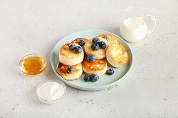 Plate with tasty cottage cheese pancakes, sour cream, honey and blueberry on light background