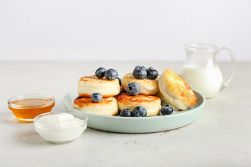 Plate with tasty cottage cheese pancakes, sour cream, honey and blueberry on table