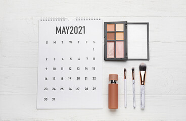 Calendar with decorative cosmetics on light wooden background