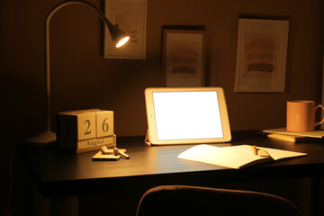 Stylish workplace with glowing lamp and tablet computer in dark room