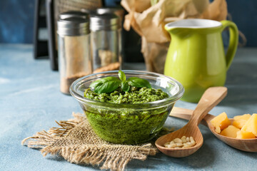 Bowl with tasty pesto sauce, cheese and pine nuts on color background, closeup
