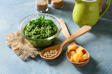 Bowl with tasty pesto sauce, cheese and pine nuts on color background, closeup