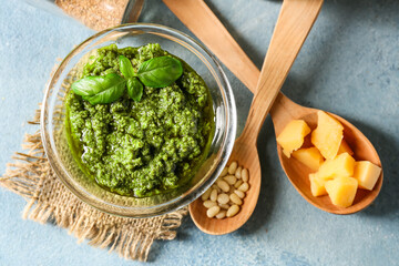 Bowl with tasty pesto sauce, cheese and pine nuts on color background, closeup