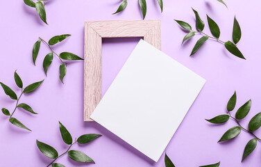 Composition with empty picture frame, blank card and green leaves on color background