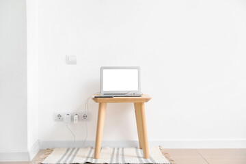 Table with charging laptop and mobile phone near light wall